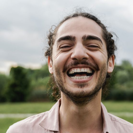 Ein junger Mann mit Bart lacht fröhlich in die Kamera